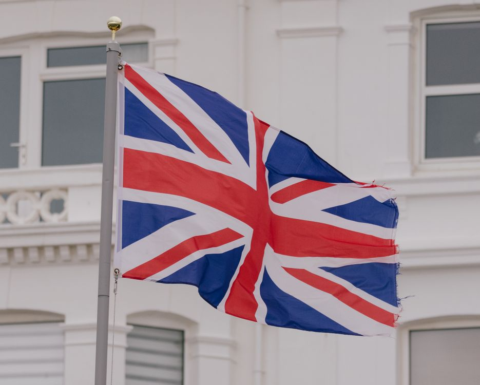 A Union Jack flag flying on a flagpole in front of a white building.